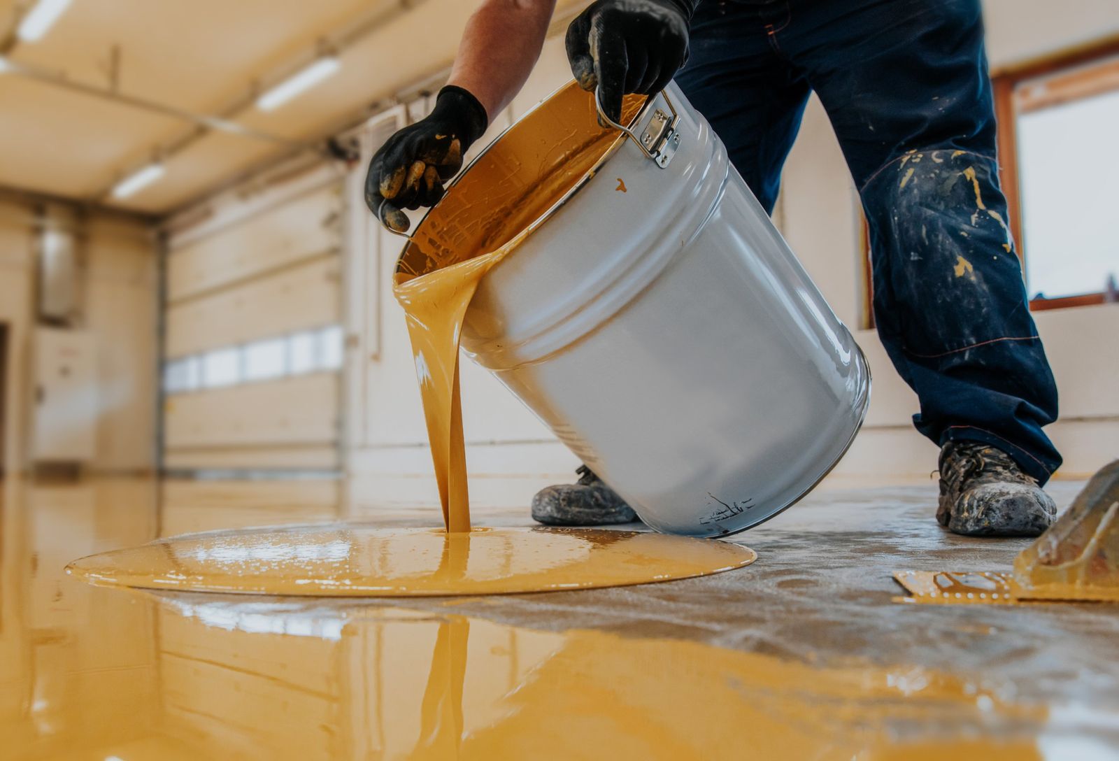 Epoxy flooring contractor pouring epoxy coating onto a prepared concrete floor