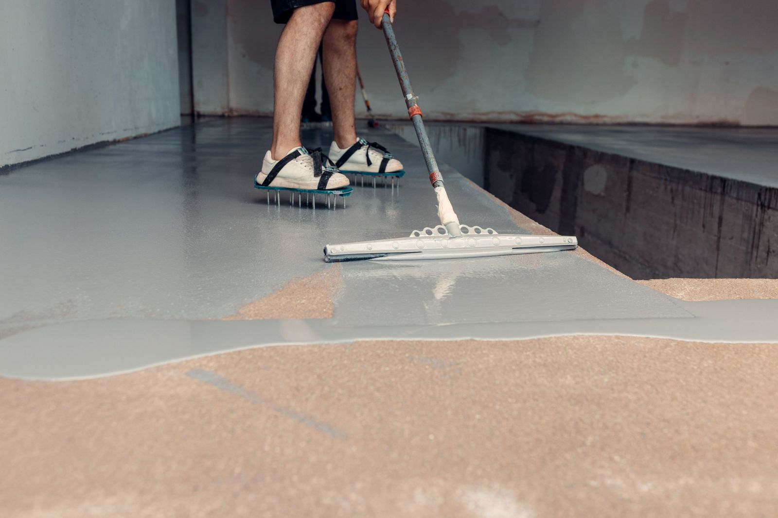 Installer applying a gray epoxy garage floor coating over diamond-ground concrete
