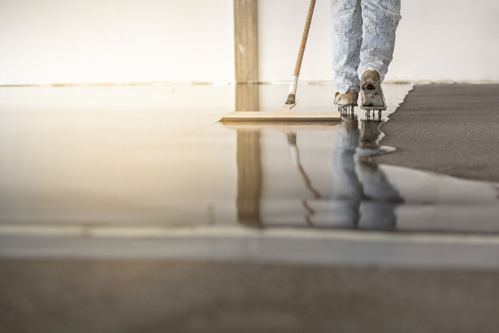 Installer spreading a clear floor coating over prepared concrete with a squeegee