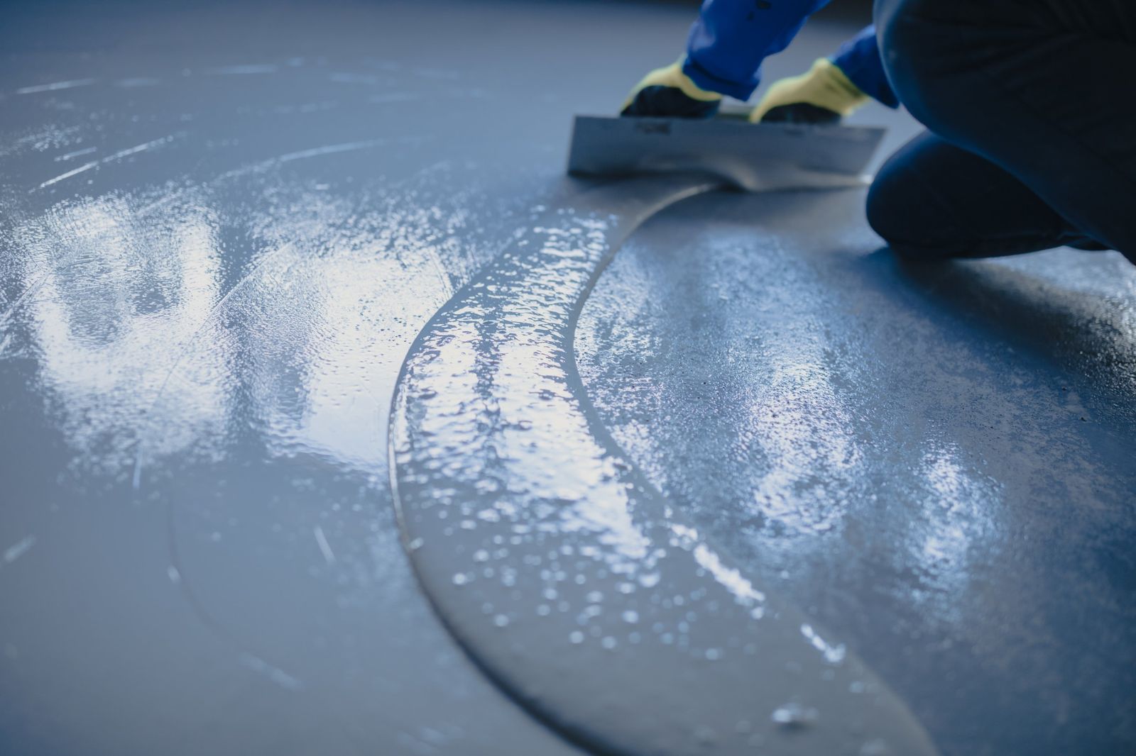 Gray floor coating being spread across a concrete slab with a trowel