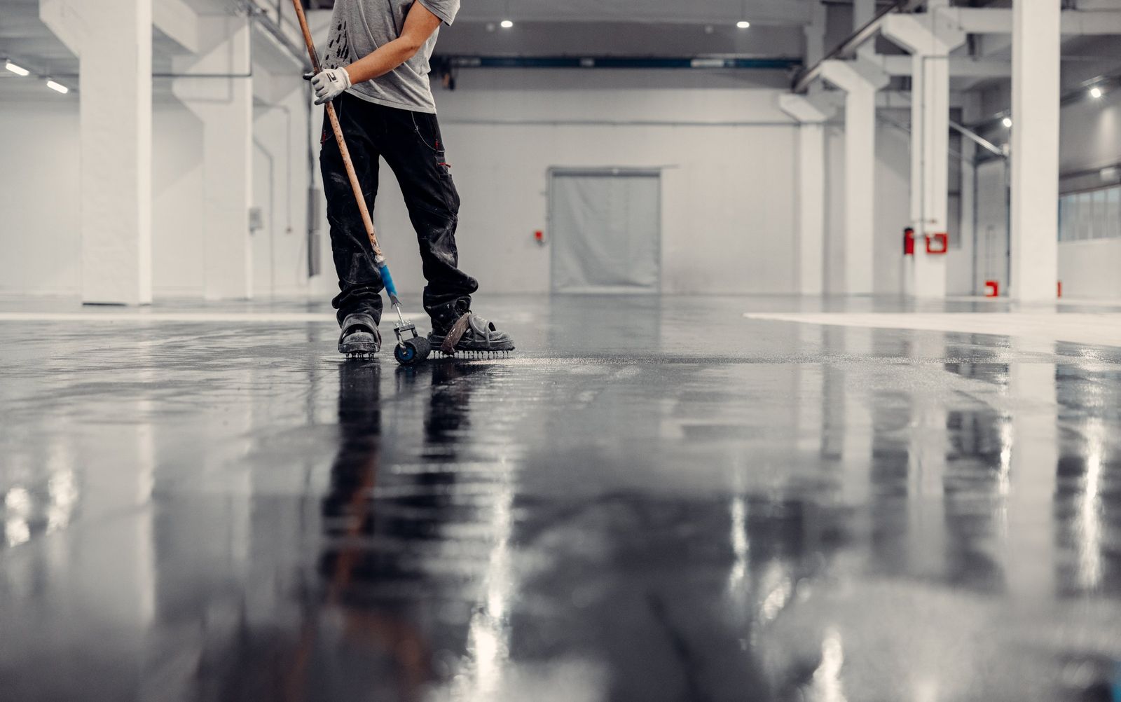 Installer in spiked shoes rolling out a self-leveling epoxy floor in a commercial building